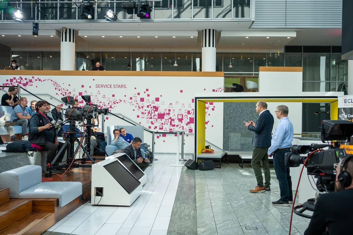 Person talking to a group of people in a public space meant for talks within the Microsoft office building. Three cameras are filming the speaker.